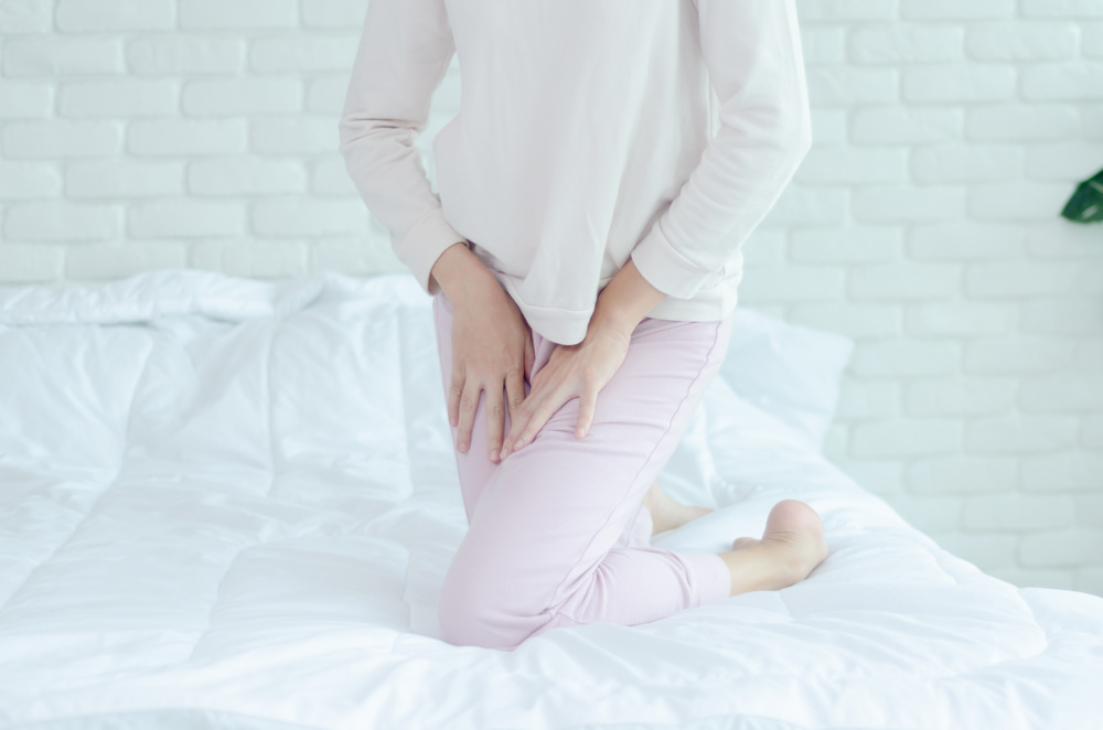 Mulher em cima da cama com as mãos entre as pernas.
