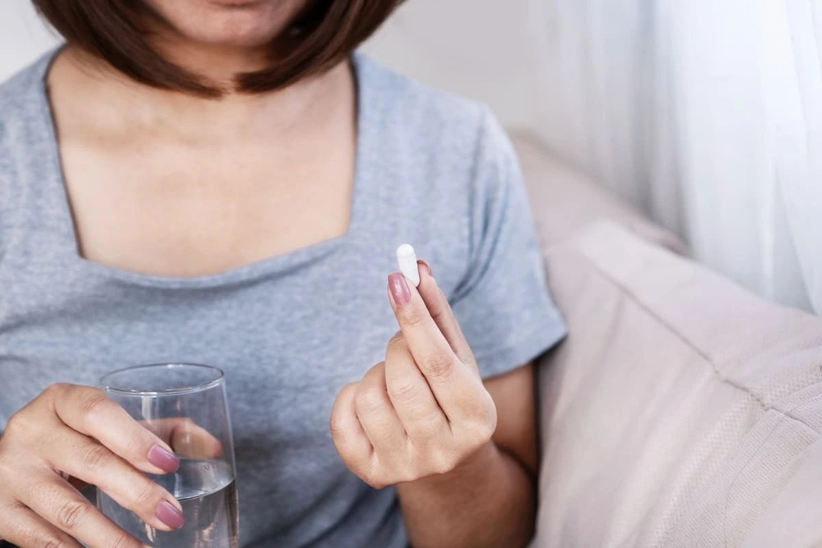 Uma mulher segura um comprimido de vitamina D em uma das mãos e um copo de água na outra, prestes a tomar o suplemento.